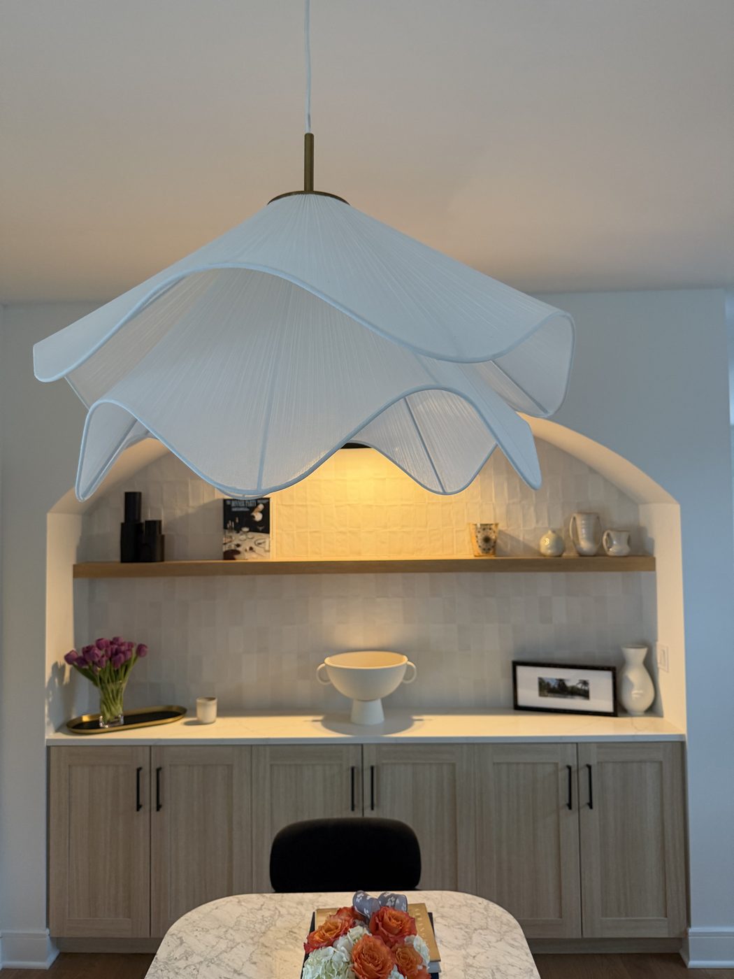 Sculptural pendant light over arched built-in with styled shelving